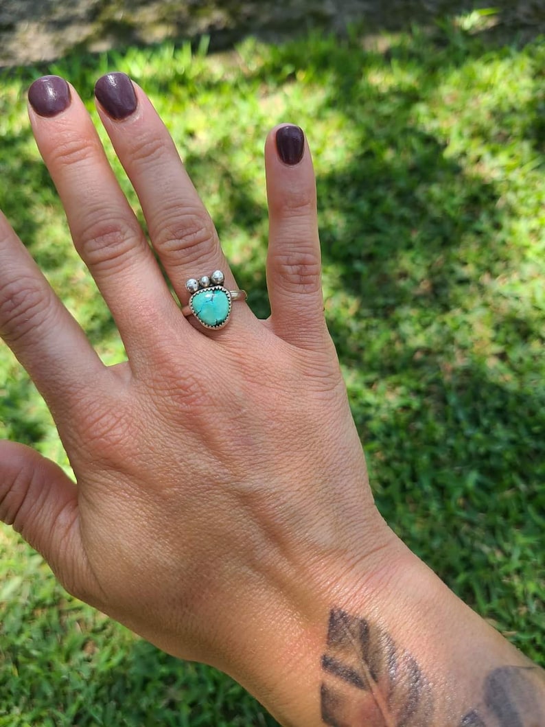 Może przedstawiać: Srebrny pierścionek z turkusowym kamieniem w kształcie serca i trzema srebrnymi koralikami na obrączce.