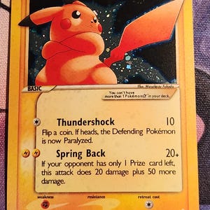 May include: A Pikachu Pokémon trading card. The card features a yellow border with the character Pikachu in the center. The card has text that reads "Thundershock" and "Spring Back". The card is from 2006.