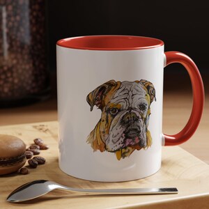 Puede incluir: Taza de cerámica blanca con borde y asa rojos. La taza presenta una ilustración de acuarela de la cara de un bulldog.