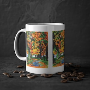 Puede incluir: Taza de café de cerámica blanca con una pintura colorida de un camino a través de un bosque con follaje de otoño. La pintura se repite en ambos lados de la taza.