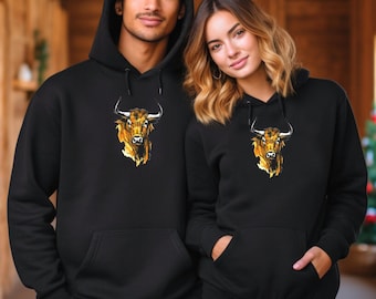 May include: Two black hooded sweatshirts. Each sweatshirt features a gold and brown bull graphic on the front. The sweatshirts have a front pocket and a hood with a drawstring. The models are wearing the sweatshirts.
