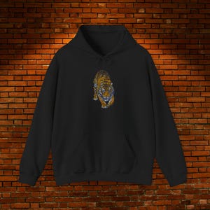 Puede incluir: Sudadera con capucha negra con una ilustración detallada de un tigre. El tigre está representado en tonos naranja, marrón y azul, mirando hacia adelante. La sudadera tiene un bolsillo de canguro y una capucha con cordón.