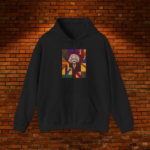 Puede incluir: Sudadera con capucha negra con un gráfico colorido de Albert Einstein. El gráfico muestra a Einstein con un traje y su pelo y bigote, rodeado de formas geométricas de varios colores. La sudadera tiene un bolsillo delantero y una capucha con cordón.