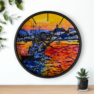 May include: A black framed clock with a colorful painting of a fishing boat in a harbor at sunset. The painting features a blue boat with a red, orange, and yellow sunset in the background.