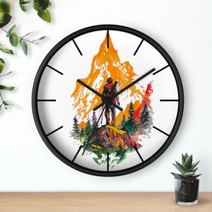 Puede incluir: Un reloj de pared negro con una esfera blanca y agujas negras. La esfera del reloj presenta una ilustración de acuarela de una persona de pie en la cima de una montaña con una puesta de sol en el fondo.