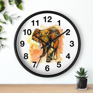 Puede incluir: Un reloj de pared con marco negro, números blancos y una ilustración de acuarela de un elefante sobre un fondo blanco.