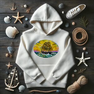Puede incluir: Una sudadera con capucha blanca con un gráfico circular de un barco navegando en un océano azul con una puesta de sol en el fondo. El gráfico es de estilo vintage con una combinación de colores amarillo, naranja y morado.