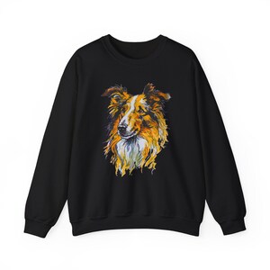 Puede incluir: Sudadera negra con una ilustración colorida de un perro Collie. El perro está mirando hacia adelante con la cabeza ligeramente inclinada hacia un lado. El pelaje del perro es una mezcla de marrón, blanco y amarillo.