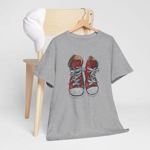 Puede incluir: Una camiseta gris jaspeada con un gráfico de zapatillas rojas de caña alta con cordones blancos.