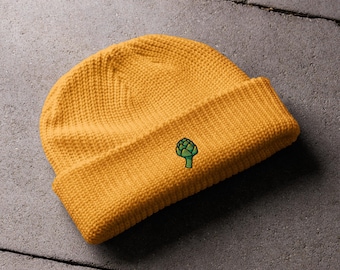 Pode incluir: Um gorro de malha amarelo com um desenho de alcachofra verde bordado.