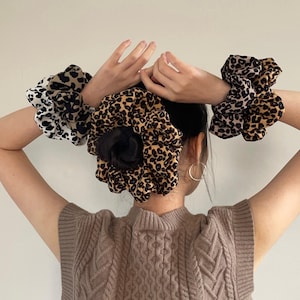 May include: Three leopard print hair scrunchies in different sizes. The scrunchies are brown, black, and white.