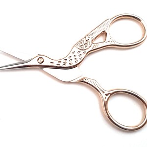 May include: Gold-toned bird-shaped scissors with a detailed design on the handle. The scissors have two loops for the fingers.