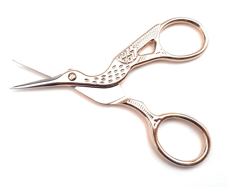 May include: Gold-toned bird-shaped scissors with a detailed design on the handle. The scissors have two loops for the fingers.