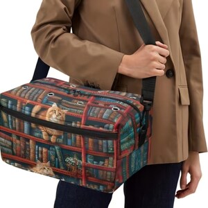 May include: A rectangular pet carrier bag featuring a vibrant print of a library bookshelf filled with numerous books and two orange tabby cats. The bag includes a black adjustable shoulder strap, a zippered top closure, and silver metal grommets.