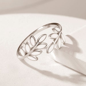 May include: A silver ring with a white enamel design of leaves. The ring is open and adjustable.