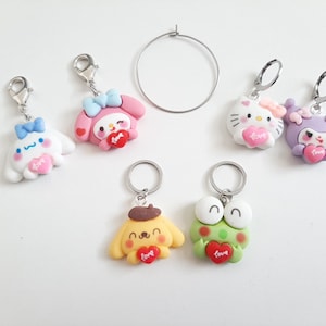 May include: A set of six keychains featuring various cartoon characters holding hearts with the word "love" on them. The characters include Hello Kitty, My Melody, Cinnamoroll, Keroppi, and two others. The keychains are made of colorful plastic and have silver metal rings.