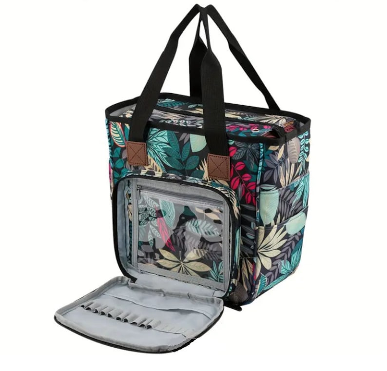 May include: A black and green tote bag with a floral print. The bag has a zippered pocket on the front and a large open pocket on the inside. The bag is open and the inside is visible.
