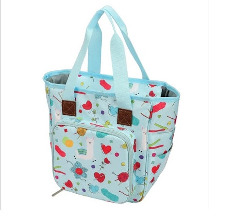 May include: A light blue tote bag with a zippered pocket and a colorful print of llamas, yarn balls, and knitting needles. The bag has two handles and a zipper closure.