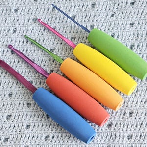 May include: A set of six colorful crochet hooks with foam handles. The handles are green, yellow, orange, red, and blue. The hooks are arranged in a rainbow pattern.