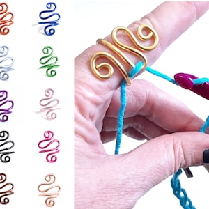 May include: A gold wire ring with a swirling design, worn on a finger holding a crochet hook and turquoise yarn.