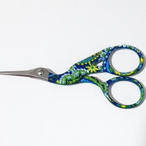 May include: A pair of blue and green patterned scissors with a long, thin blade. The scissors have a floral design and are made of metal.