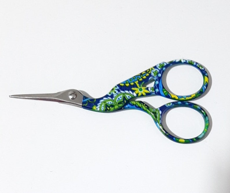 May include: A pair of blue and green patterned scissors with a long, thin blade. The scissors have a floral design and are made of metal.