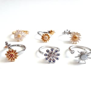 May include: Six silver and gold rings with floral and sun designs. The rings feature a variety of flowers, including daisies, sunflowers, and a stylized sun with a pearl center.
