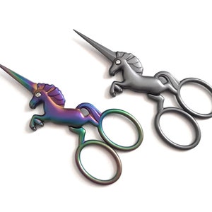 May include: Two pairs of unicorn-shaped scissors. One pair is silver, and the other pair is iridescent with rainbow colors.