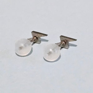 May include: A pair of silver earrings with white pearl-like spheres and lightning bolt-shaped accents.
