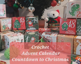 May include: A collection of square cardboard boxes featuring numbered Christmas-themed illustrations, including a green dinosaur, Santa Claus, and reindeer. A ball of green yarn and a crochet hook are positioned in front of the boxes.