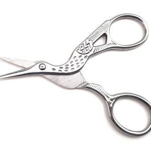 May include: Silver-toned bird-shaped scissors with a decorative design on the handles. The scissors have a pointed tip and a small round hole near the beak.