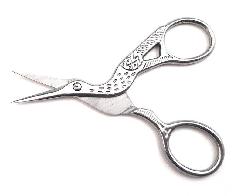 May include: Silver-toned bird-shaped scissors with a decorative design on the handles. The scissors have a pointed tip and a small round hole near the beak.