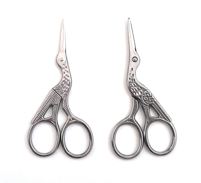 May include: A pair of silver-toned scissors with a bird design. The scissors have a detailed design and are closed.