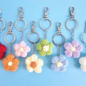 May include: Nine crocheted flower keychains in various colors, including red, orange, yellow, green, pink, purple, and white, attached to silver key rings.