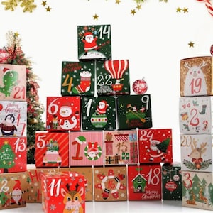 May include: A Christmas advent calendar made of cardboard boxes with festive illustrations and numbers from 1 to 24. The boxes are stacked in a pyramid shape, with a Christmas tree and a reindeer on the bottom row.