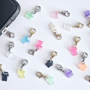 May include: Assortment of colourful charms with various shapes and designs. The charms are attached to silver and gold clasps. The charms are perfect for adding a personal touch to bags, keychains, and other accessories.