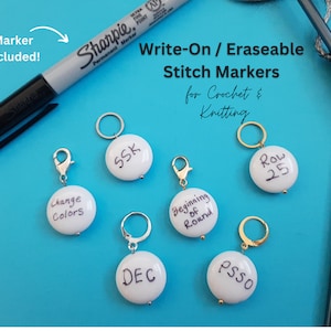 May include: White, write-on stitch markers for crochet and knitting. Each marker has a silver or gold-coloured clasp or ring. The markers are labelled with terms like "SSK", "DEC", and "Change Colors". A black marker is included.