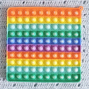 May include: A rainbow-colored pop-it fidget toy with 100 individual bubbles numbered 1 to 100. The toy is made of silicone and has a light orange border.