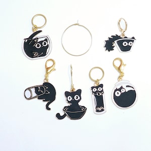 May include: Set of seven black cat charms with gold accents. The charms feature different designs, including a cat in a bowl, a cat in a fishbowl, a cat in a jar, and a cat with a fishbone. The charms are perfect for adding a touch of whimsy to your jewelry or crafts.