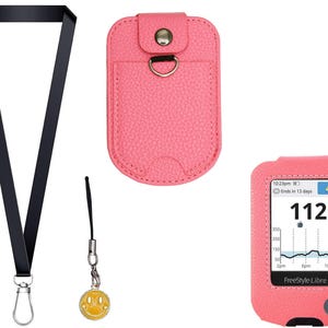 May include: Accessories for a Freestyle Libre 3 glucose monitor. The image shows a black lanyard, a pink leatherette case, a smiley face charm, and a pink protective case with the monitor displaying a blood glucose reading of 112 mg/dL.