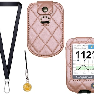 以下が含まれることがあります： ローズゴールドのキルティングケースと、シルバーの留め金が付いた黒いストラップ。 Freestyle Libre 3血糖値モニターは112 mg/dLの数値を表示します。 小さなスマイリーフェイスのチャームが黒いコードからぶら下がっています。