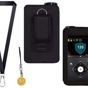 Könnte beinhalten: Ein schwarzes Schlüsselband mit Silberverschluss, ein gelber Smiley-Anhänger und eine schwarze Lederhülle für ein medizinisches Gerät. Der Bildschirm zeigt einen Blutzuckerwert von 120 mg/dL an.