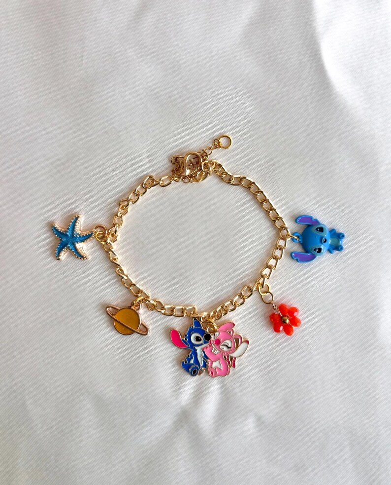May include: Gold-colored charm bracelet featuring colorful enamel charms. Charms include a blue starfish, a yellow planet, a blue and pink cartoon couple, a red flower, and a blue cartoon character.