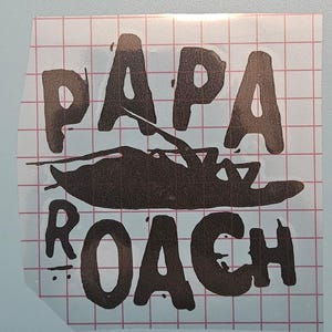 May include: A dark brown sticker with the words "PAPA" above a cockroach illustration and the word "ROACH" below. The sticker is on a grid-patterned background.