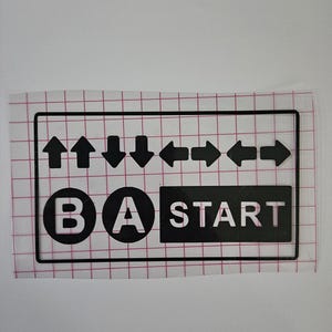 May include: Black vinyl decal featuring a rectangular design with directional arrows, the letters B and A inside circles, and the word START. The decal is on a clear, grid-patterned backing.