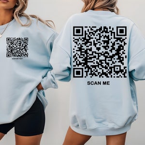 May include: Two light blue sweatshirts with a black QR code printed on the front and back. The front sweatshirt has the text "CUSTOM TEXT" below the QR code. The back sweatshirt has the text "SCAN ME" below the QR code.