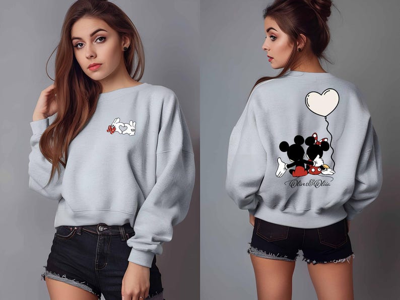 May include: Light gray sweatshirt featuring a cartoon design on the front and back. The front has a white rabbit forming a heart with its hands and a red flower. The back has Mickey and Minnie Mouse with a heart balloon.