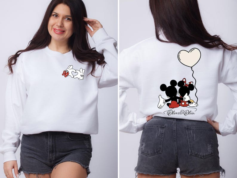 May include: White sweatshirt featuring Mickey and Minnie Mouse graphics. The front displays Mickey's hands forming a heart with a red bow. The back shows Mickey and Minnie with a heart balloon. The text "Oliver & Olivia" is below.