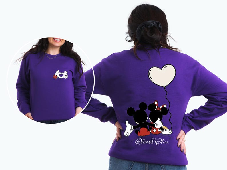 May include: A purple sweatshirt featuring a Mickey and Minnie Mouse design. The back of the sweatshirt shows the couple embracing under a heart-shaped balloon. The front has a hand-heart design with a red flower.