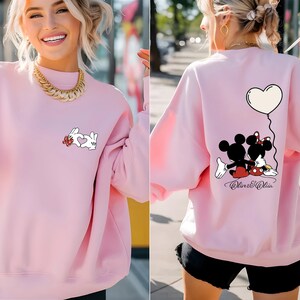 May include: A light pink sweatshirt featuring a white rabbit design with a heart on the front. The back of the sweatshirt has a Mickey and Minnie Mouse graphic with a heart-shaped balloon. The text "Oliver & Olivia" is below the characters.